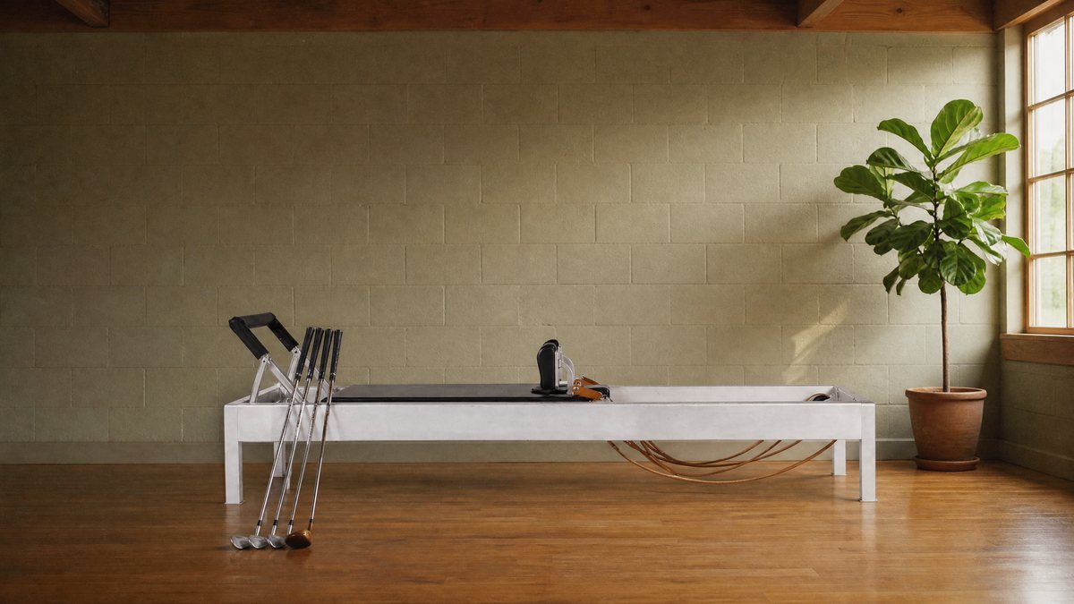 Classical Pilates reformer in a West Hollywood studio with golf clubs leaning against it and a fiddle leaf fig by the window