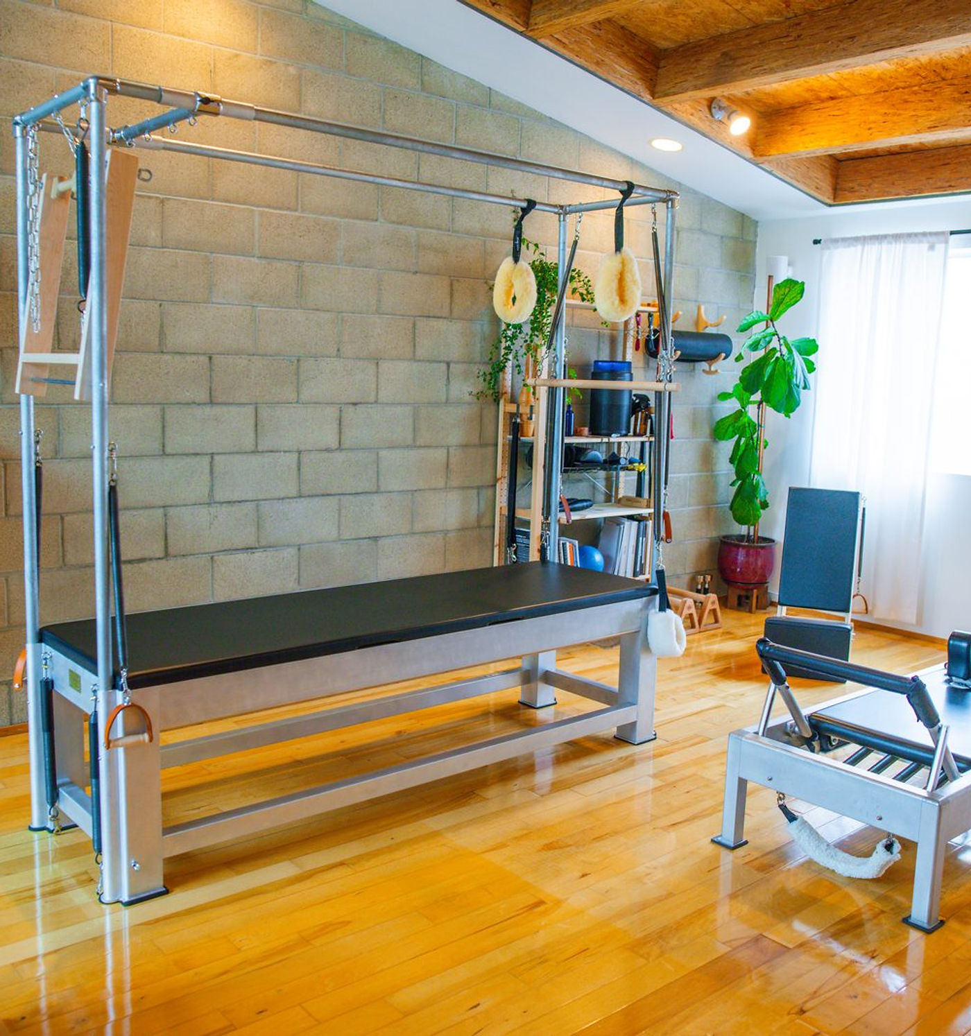 A Cadillac trapeze table and a reformer in the sunlit studio, beside a tall window